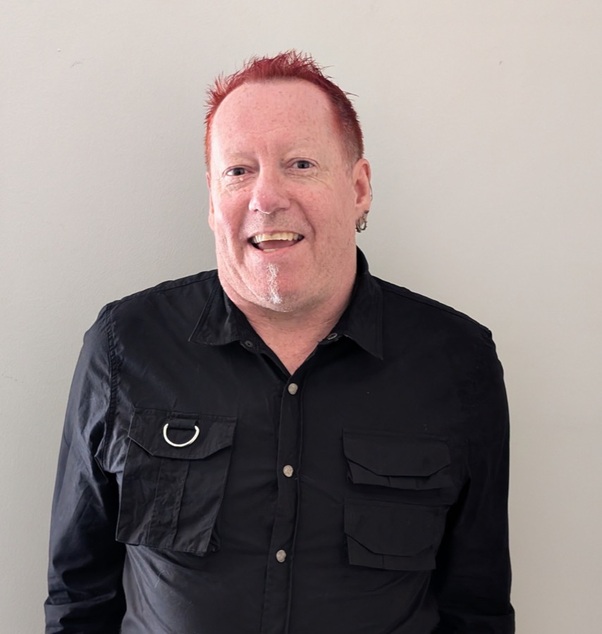 Nigel McLaughlin smiling, wearing a black shirt, with bright red spiky hair.